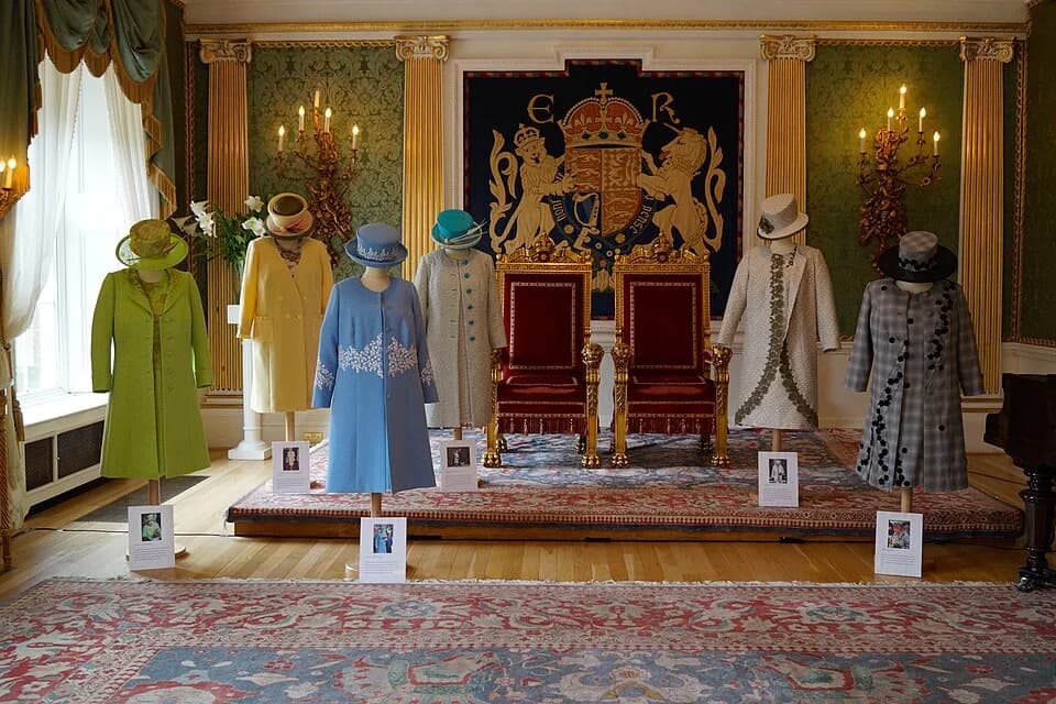 Elizabeth II - "Five of the six outfits on display and all six hats were designed by Angela Kelly LVO, personal assistant and senior dresser to The Queen since 2002. The sixth outfit was designed by K
