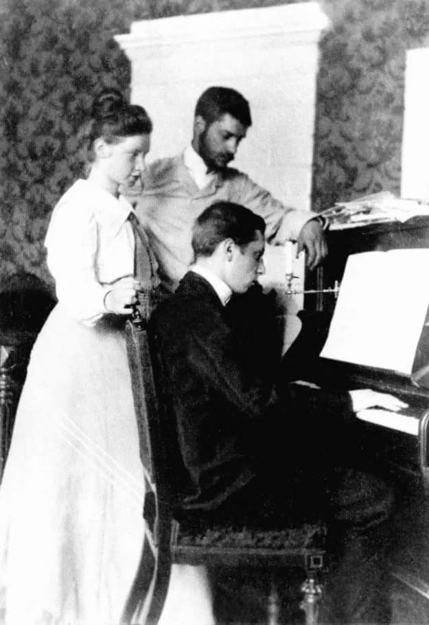 Igor Stravinsky - Igor Stravinsky seated at the piano. Standing from left to right: Yekaterina Nosenko (Stravinsky's cousin and future wife) and the composer's brother Gury.