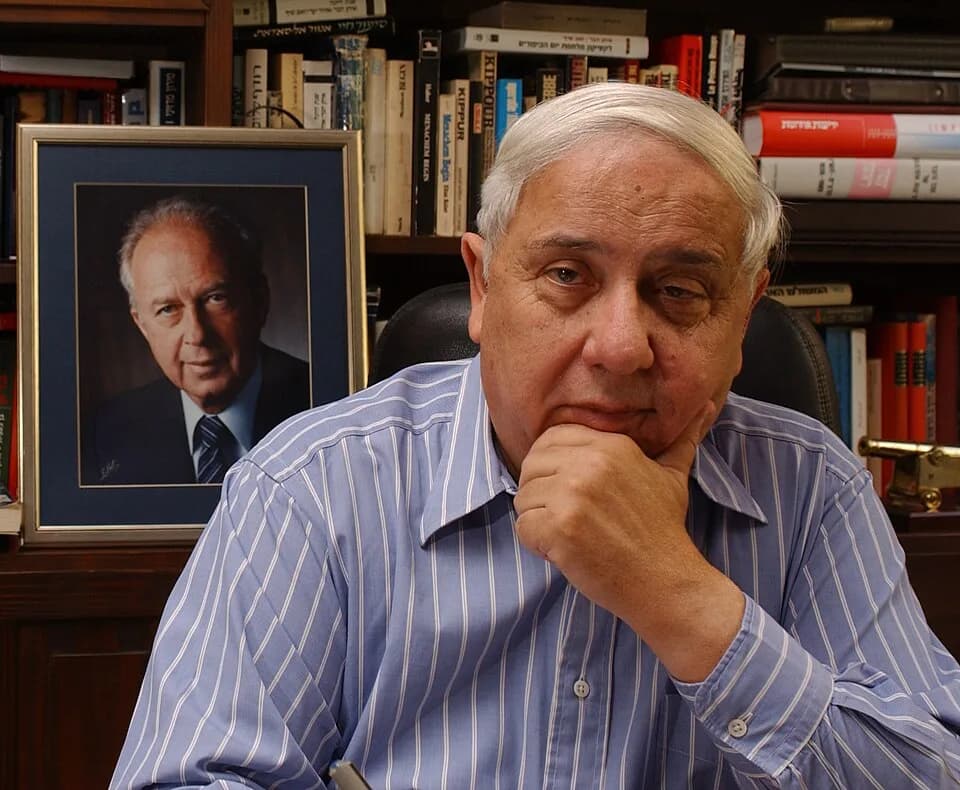Yizhak Rabin - Eitan Haber, with a portrait of Yitzhak Rabin behind him.