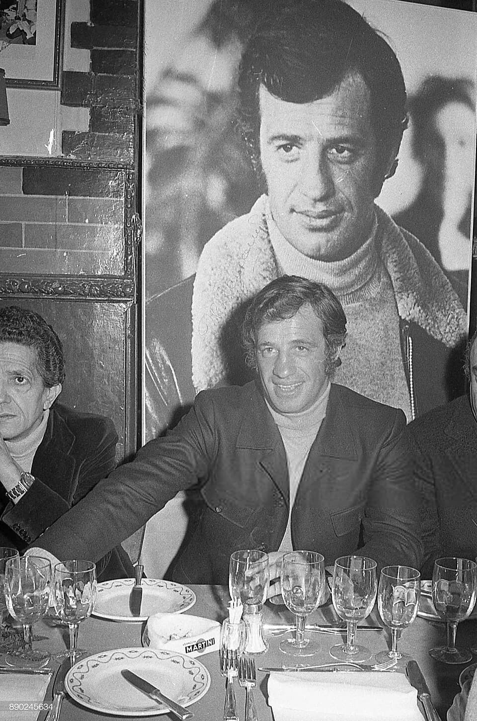 Jean-Paul Belmondo - L'acteur français Jean-Paul Belmondo  lors d'un dîner à Rome, le 12 septembre 1971, à l'époque de la sortie du film Le Casse. Son image dans le film est affichée derrière lui.