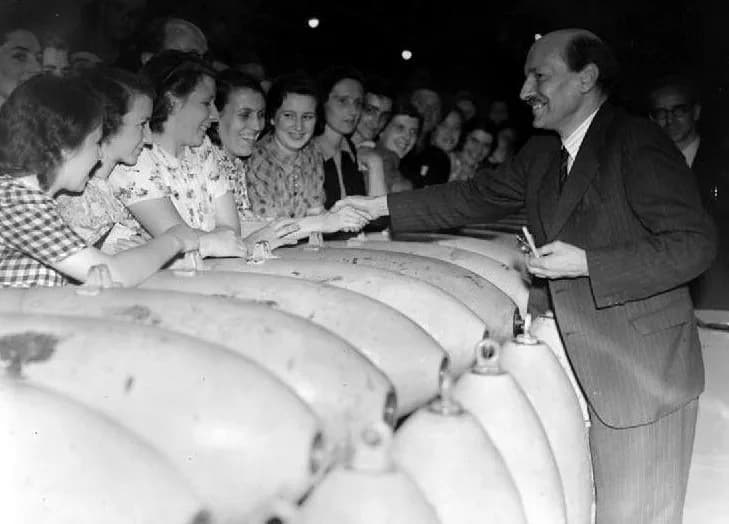 Clement Attlee - Lord Privy Seal Clement Attlee smiles as he shakes hands with cheering workers during a visit to ROF Hereford on Friday 11 July 1941. He is leaning over a pile of shells to greet the 