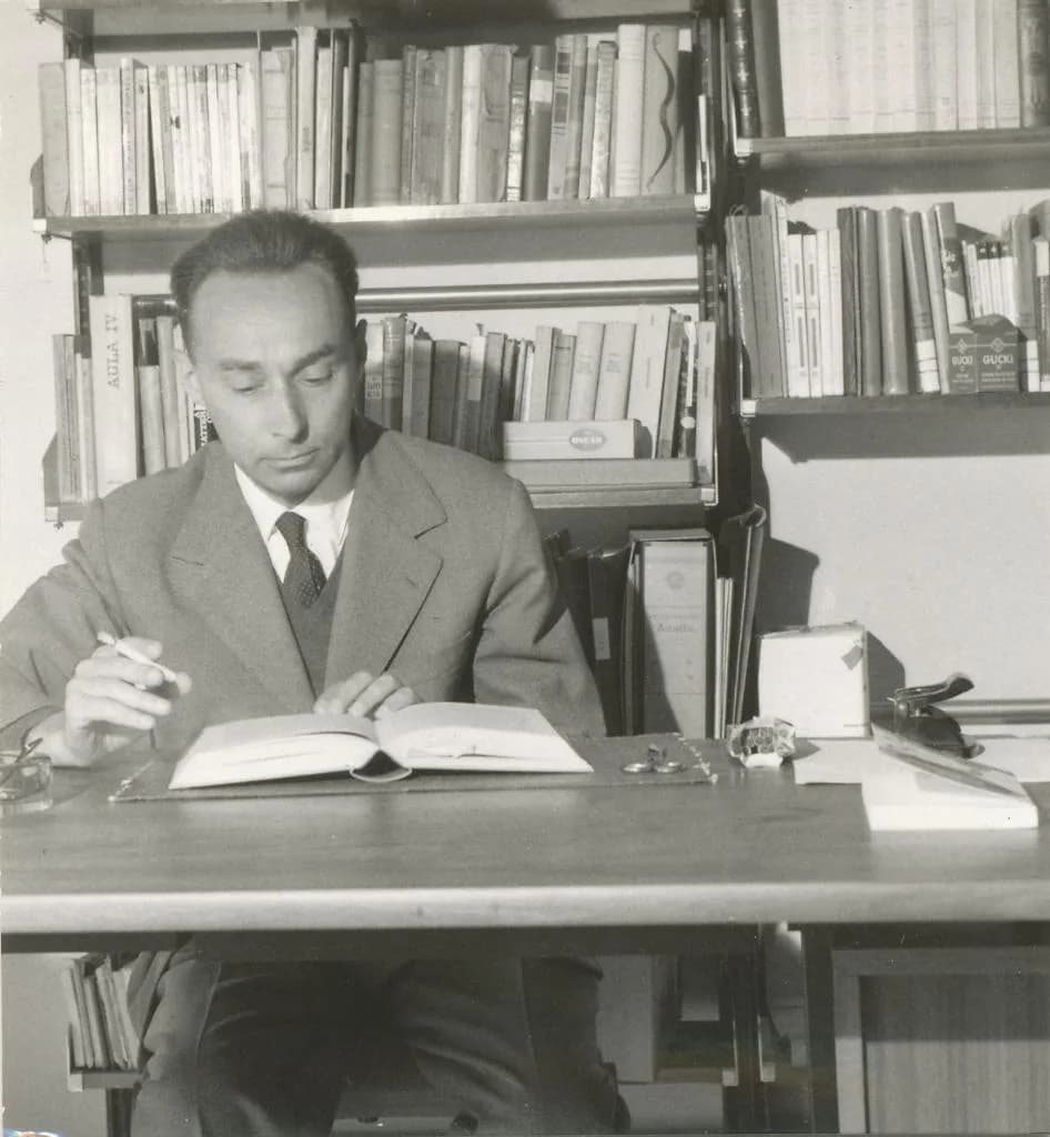 Primo Levi - Primo Levi seduto alla scrivania mentre legge con una sigaretta in mano - sullo sfondo scaffali con libri, circa 1960