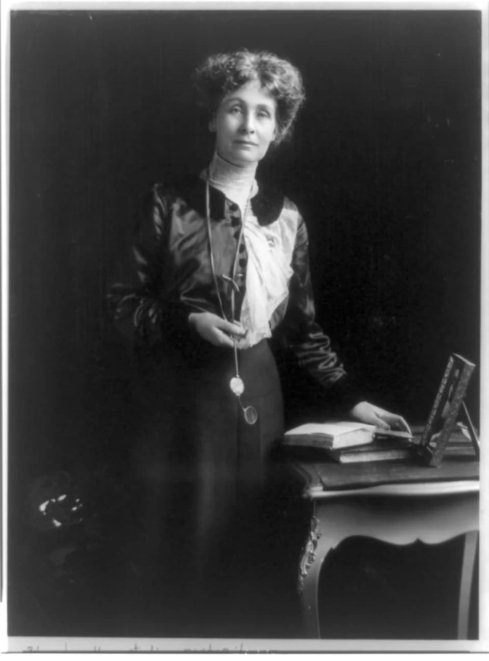 Emmeline Pankhurst - Emmeline (Goulden) Pankhurst, three-quarter length portrait, standing by small table, facing right, with left hand on book