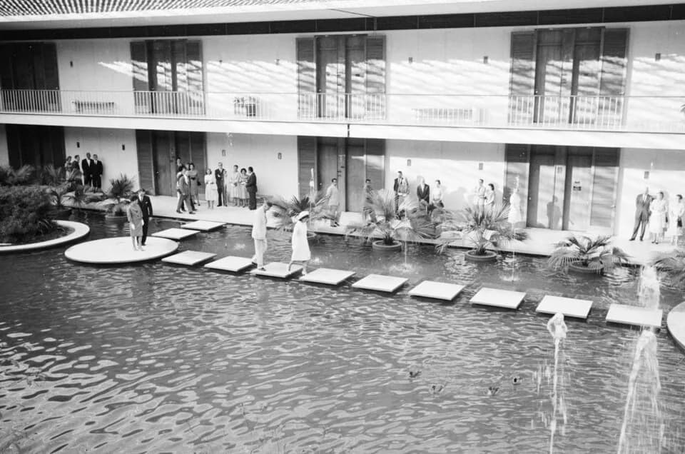 John Kenneth Galbraith - First Lady Jacqueline Kennedy walks across a courtyard pool at the Chancery of the United States Embassy in New Delhi, India. US Ambassador to India, John Kenneth Galbraith, w