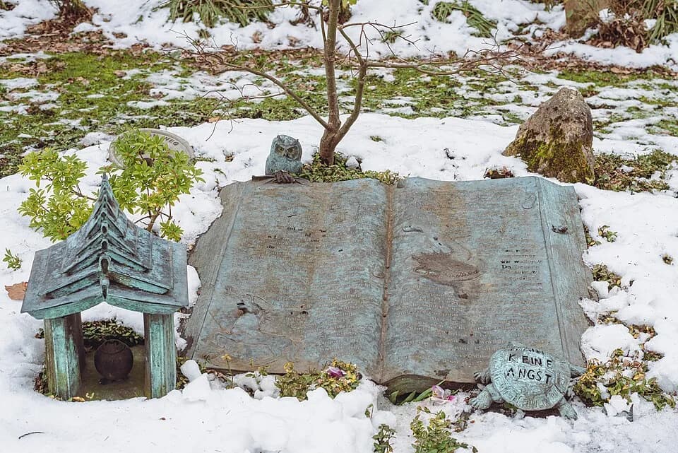 Michael Ende - Detailed view of the grave of Michael Ende on the Munich Woodland Cemetery, Germany. To the left of the big book is a small temple made from open books. On the top of the left page of t