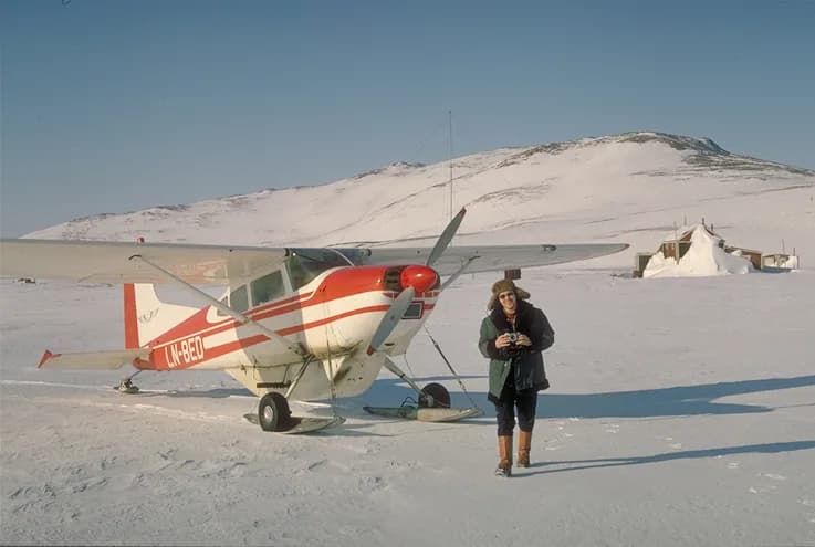 Erik the Red - Cessna 185 fitted with ski mounts parked on the snow in front of the old Norwegian fishing and telegraph station in Myggbukta, Myggebugten.