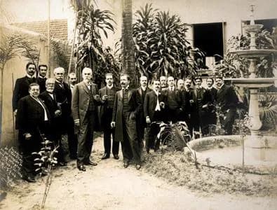 Machado de Assis - Machado de Assis (seg. do canto esquerdo, de terno preto) com grupo de intelectuais (jornalistas, escritores e artistas cariocas).