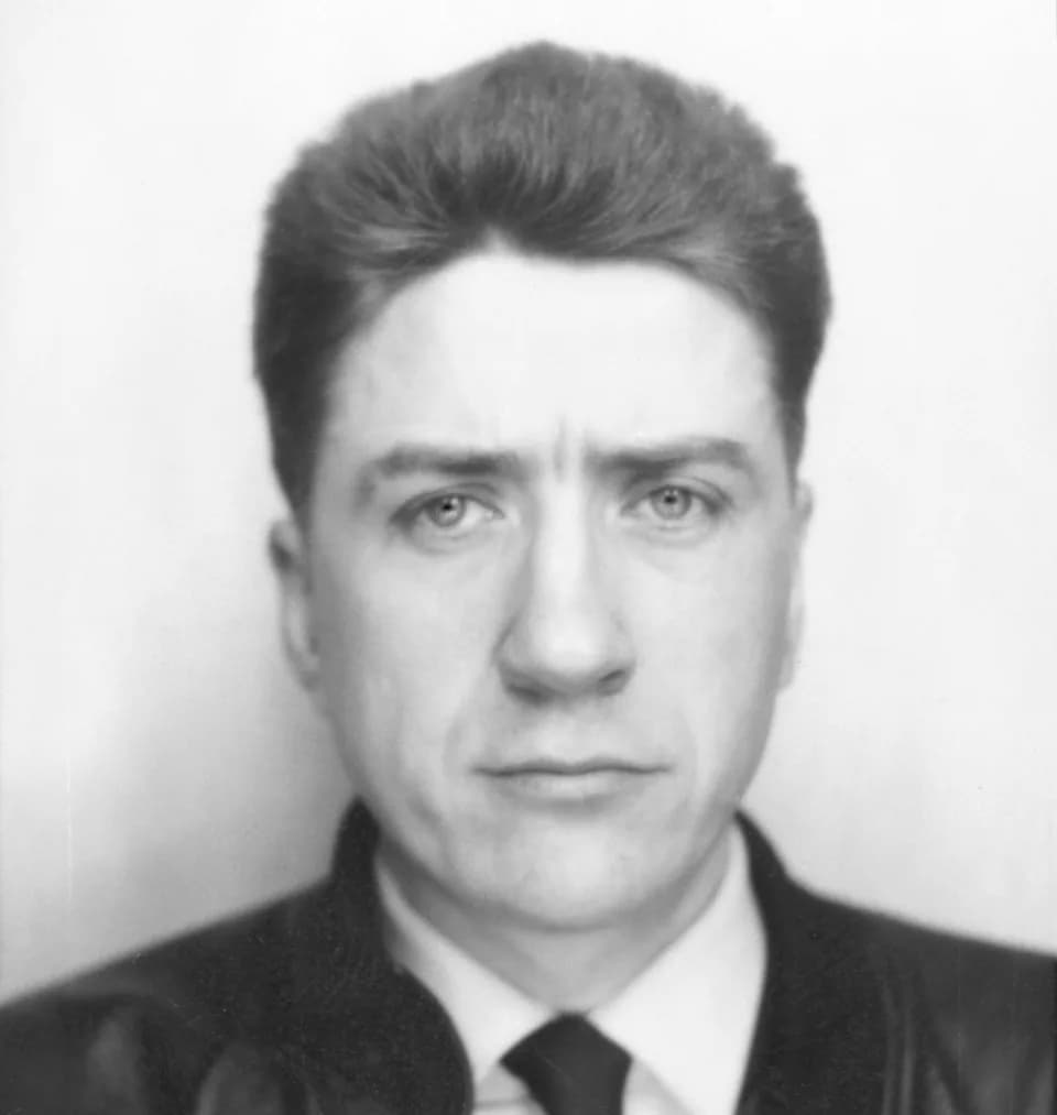 Alain Resnais - Alain Resnais fixe l'objectif sans émotion particulière, fronçant légèrement les sourcils. Il porte les cheveux bruns courts, coiffés en arrière. Il est vêtu d'un veston sombre, d'une 