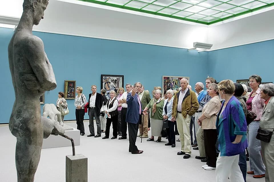 Max Beckmann - Christian von Holst in einem Ecksaal der Neuen Staatsgalerie von James Stirling zwischen Gemälden von Max Beckmann und Wilhelm Lehmbrucks kriegsversehrtem "Emporsteigendem Jüngling" von
