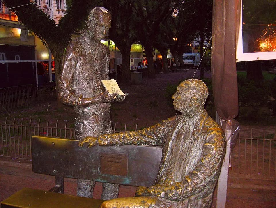 Jean Genet - Two Poets.  Standing, Carlos Drummond de Andrade.  Sitting, Mário Quintana.  
Drummond had a metal book in his hands, which was stolen.  People now always put a book in his hands.  The on