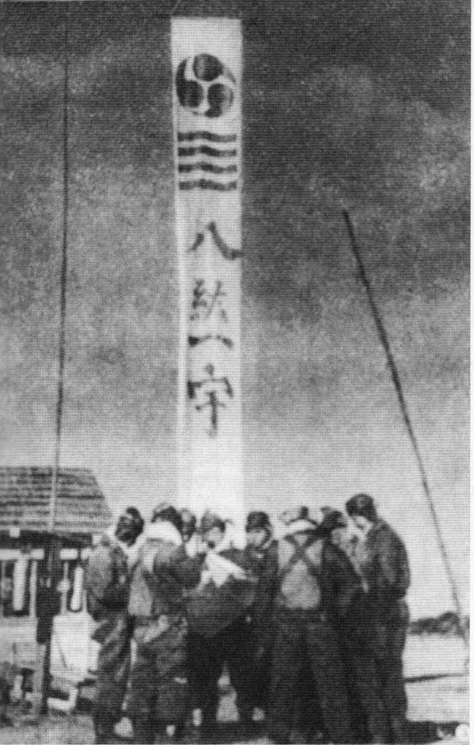 Jimmu - 日本航空隊基地に掲げられた「八紘一宇」の旗印と航空兵。「八紘一宇」とは引用元のキャプションによれば「肇国の精神にのっとた八紘一宇の実現」として戦争遂行のスローガンになっていたという。