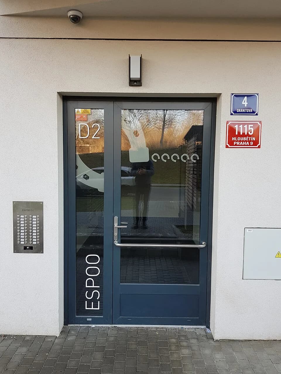 Ragnar Granit - Vchod do domu čp. 1115/4, ulice Granitova, Praha 9 - Hloubětín, projekt Espoo (součást Suomi Hloubětín), budova D2. Na dveřích je vyznačen projekt (Espoo), budova (D2) a podkovy.