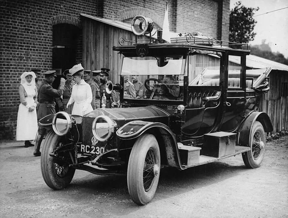 Mary of Teck - Queen Mary arriving at a hospital. She is met by a welcoming party of army officials. One nurse stands in the background watching the scene. The Queen has just alighted from a Rolls Roy