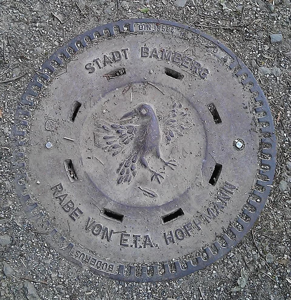 E. T. A. Hoffmann - Schachtdeckel  der Stadt Bamberg am Wanderweg an der Regnitz mit dem Raben von E.T.A. Hoffmann
