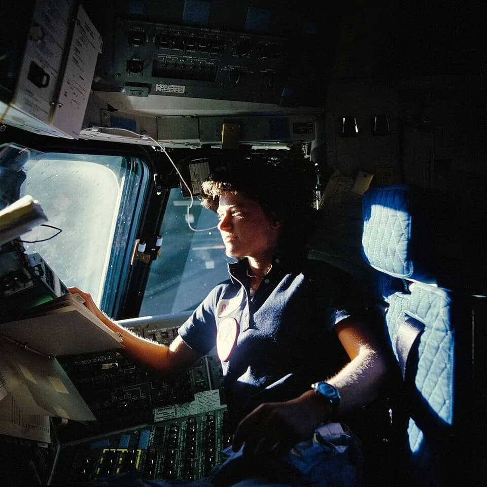 Sally Ride - Astronaut Sally K. Ride, mission specialist on STS-7, monitors control panels from the pilot's chair on the Flight Deck. Floating in front of her is a flight procedures notebook.