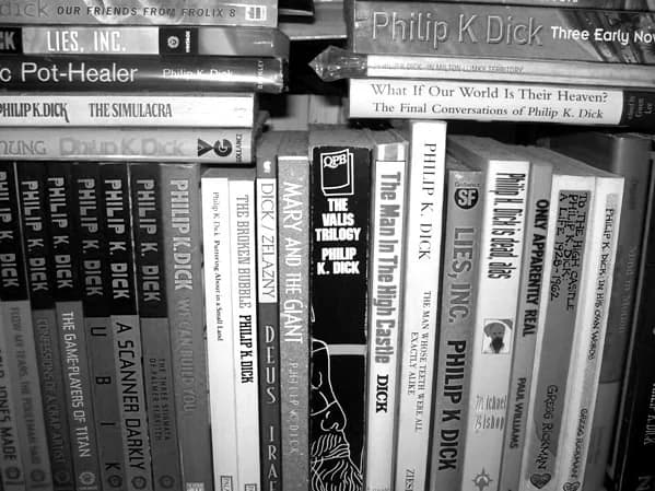 Philip K. Dick - Black and white photograph of a shelf of books by and about Philip K. Dick, showing the spines only