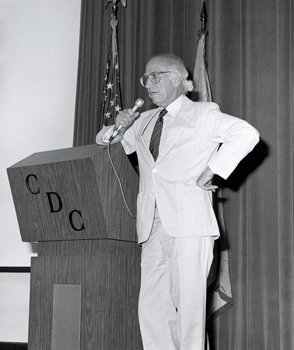 Jonas Salk - Standing at the podium during his 1988 Centers for Disease Control visit, this photograph showed Dr. Jonas Salk, creator of the first polio vaccine in 1955, fielding questions during his 