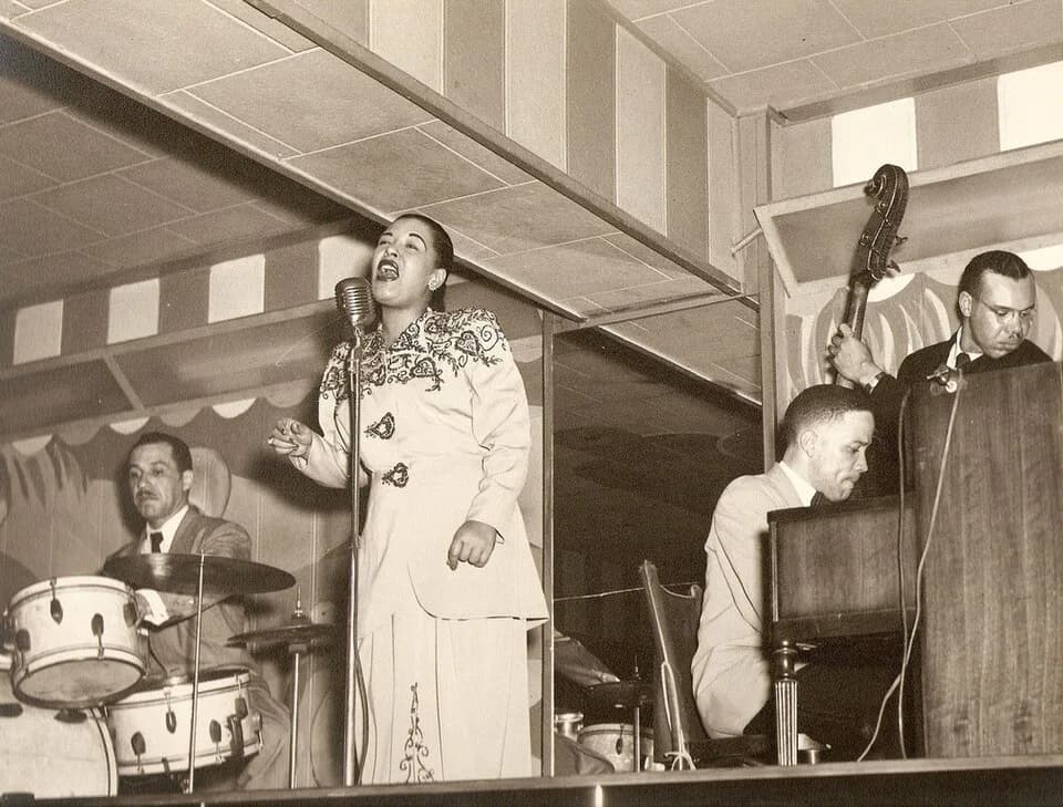 Billie Holiday - possibly Al Dunn (drums), Billie Holiday (singing), Bobby Tucker (piano), unknown (double-bass).
Original caption: "Billie at the Club Bali, Washington with Al Dunn (drums), Bobby Tuc