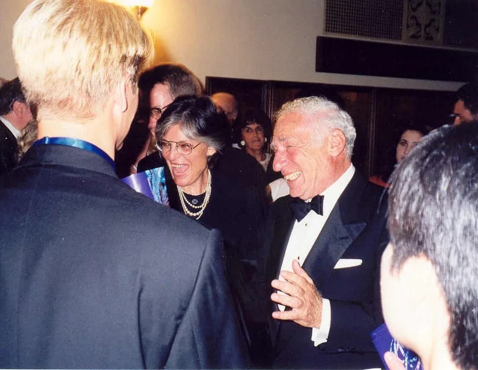 Anne Bancroft - Anne Bancroft and Mel Brooks talking to Bette Midler who is obscured by the man on the left. The photo has been taken at the 49th Emmy Awards in 1997.