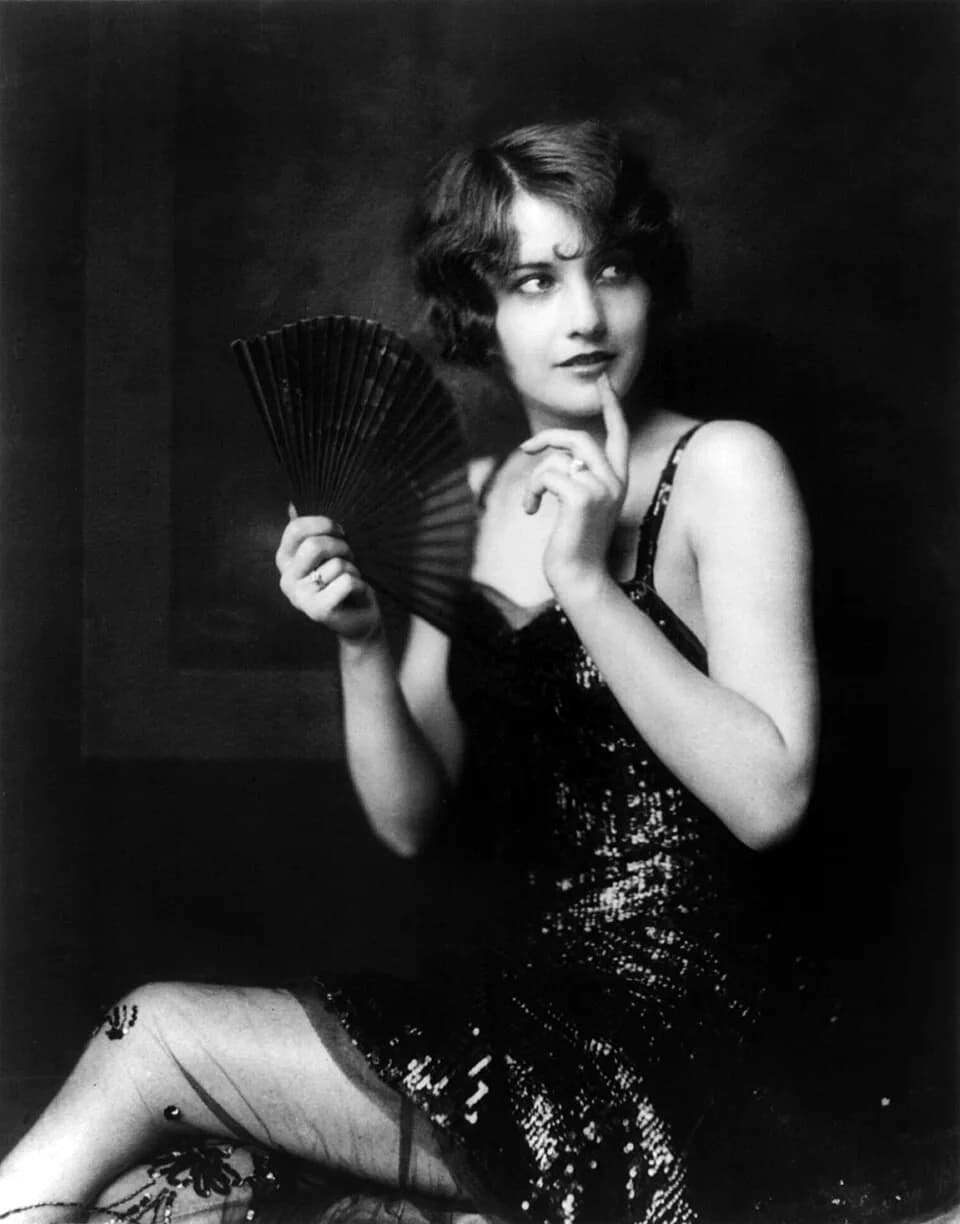 Barbara Stanwyck - Future Hollywood star Barbara Stanwyck, three-quarter length portrait, seated, turned to the left, holding fan.