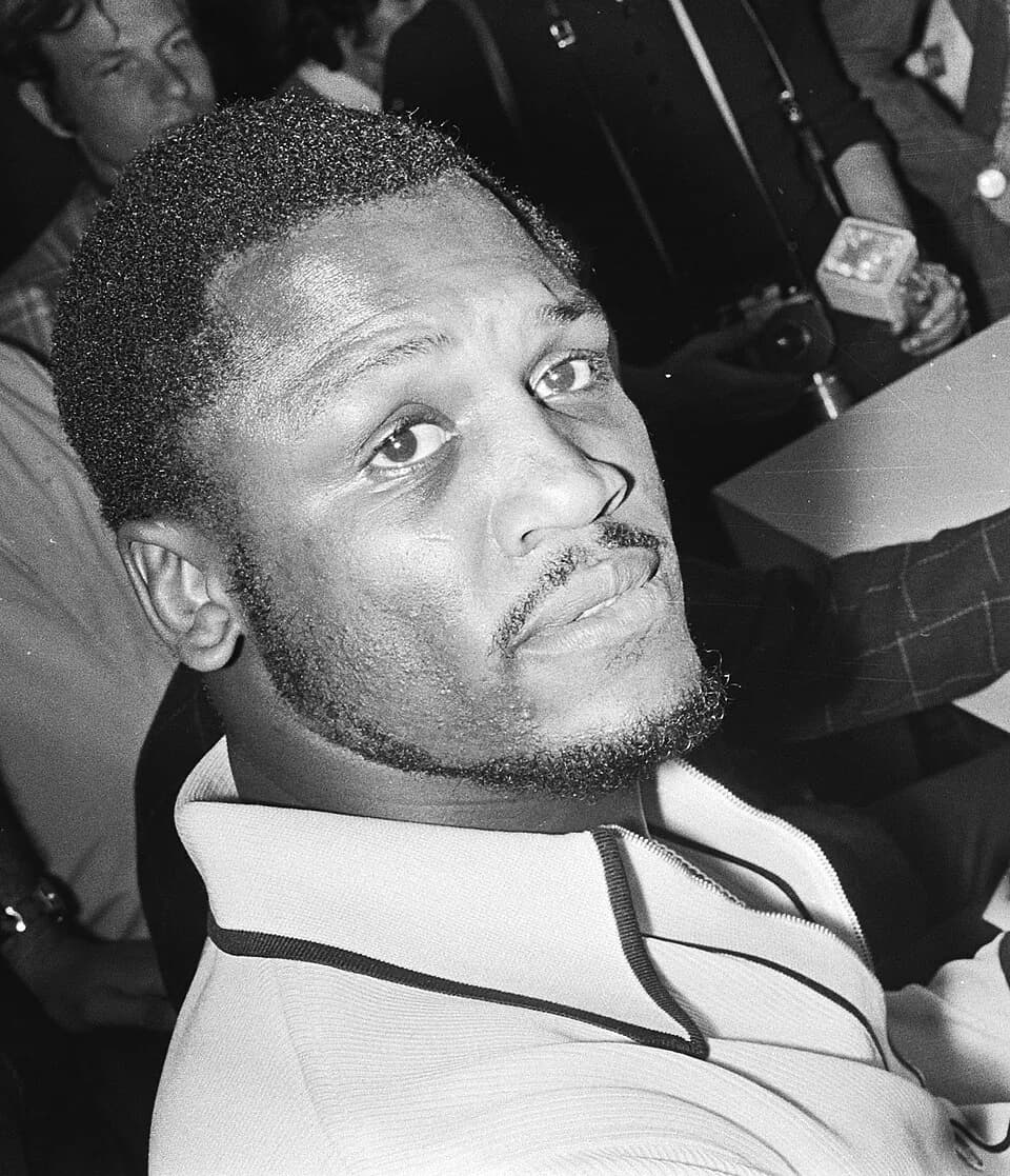 Joe Frazier - Joe Frazier reading Dutch newspaper about his singing career at Amsterdam Airport Schiphol (cropped)