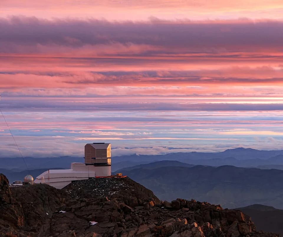 Vera Rubin - The Vera C. Rubin Observatory is shown here amidst a colorful display of clouds around sunrise.