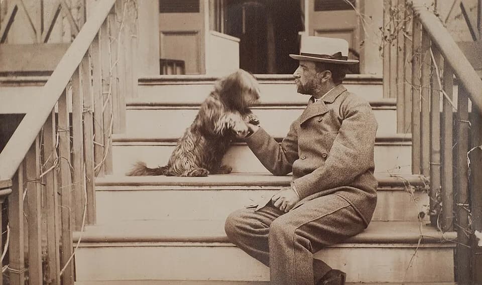 Henry Adams - Henry Adams seated with dog on steps of piazza. Photograph by Marian Hooper Adams, circa 1883. Album page:  17.4 cm x 25.2 cm;  image: 11.7 cm x 19.3 cm. From the Marian Hooper Adams pho