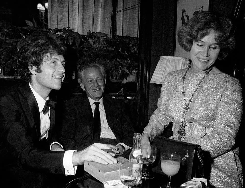 Joe Dassin - American-born French singer Joe Dassin smoking a cigar at the table of a bar. Beside him, his father, American director Jules Dassin and his mother Beatrice Launer. Paris, 1970.