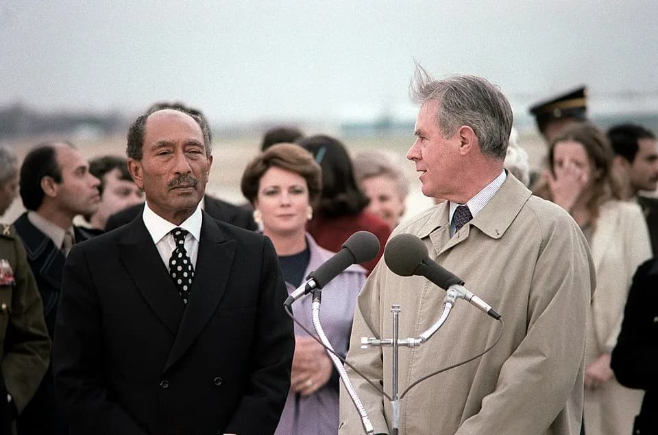 Anwar Sadat - Secretary of State Cyrus Vance welcomes President Anwar Sadat of Egypt and members of his party upon their arrival in the United States for a visit. The woman in the background wearing m