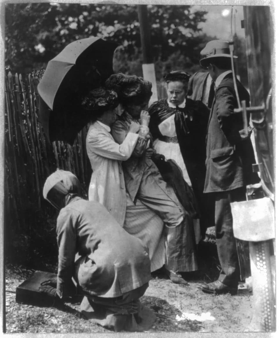Emmeline Pankhurst - Emmeline Goulden Pankhurst, 1858-1928. Full length, seated on lap of woman holding umbrella, facing right; at time of her re-arrest, May 26, 1913.