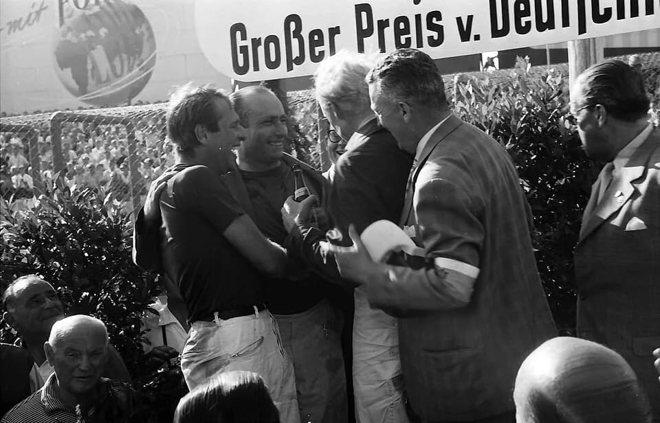 Mike Hawthorn - Third-placed driver Peter Collins (left), race winner Juan Manuel Fangio (centre left), and second-placed driver Mike Hawthorn (centre right, blond hair) celebrate together on the podi