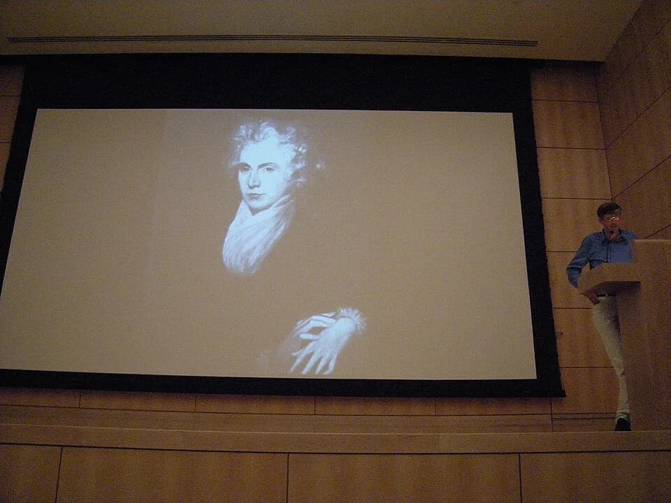 Mary Wollstonecraft - Artist Matthew Buckingham speaking at the Henry Art Gallery, Seattle, Washington. Most of this image is take up by a projected slide of John Opie's portrait of Mary Wollstonecraf