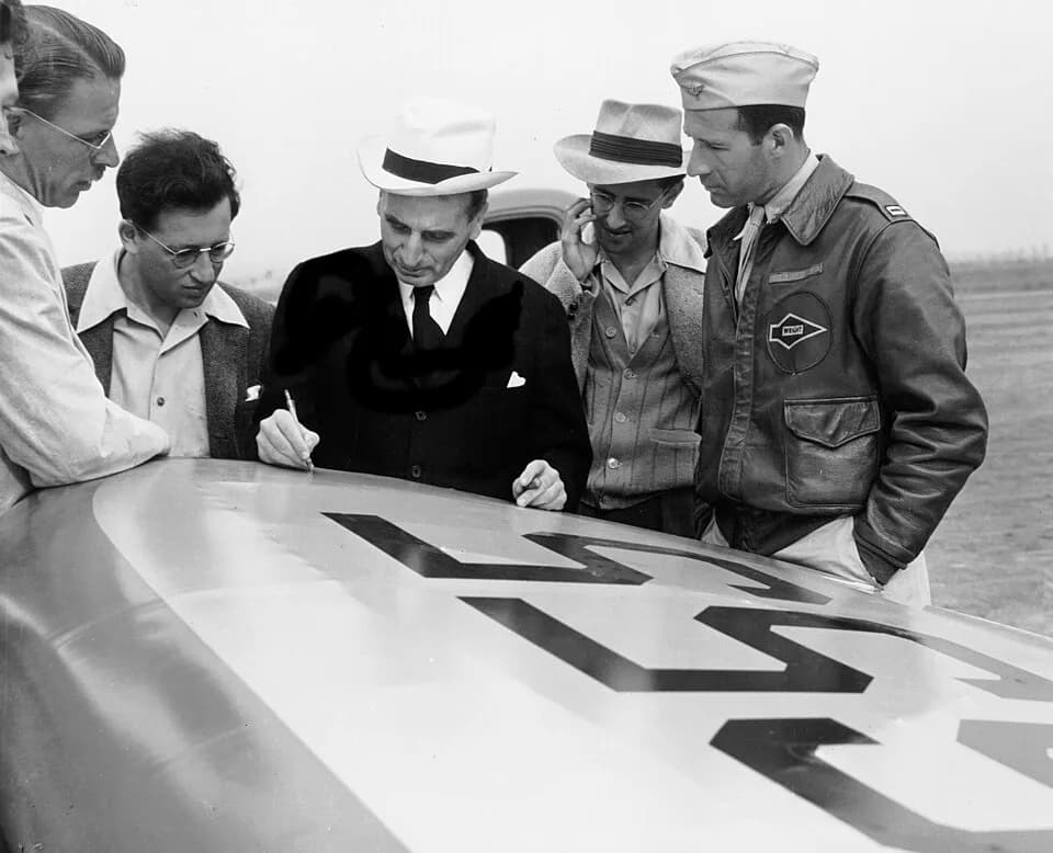 Theodore von Kármán - Dr. Theodore von Kármán (black coat) sketches out a plan on the wing of an airplane as his JATO engineering team looks on.
From left to right: Dr. Clark B. Millikan, Dr. Martin